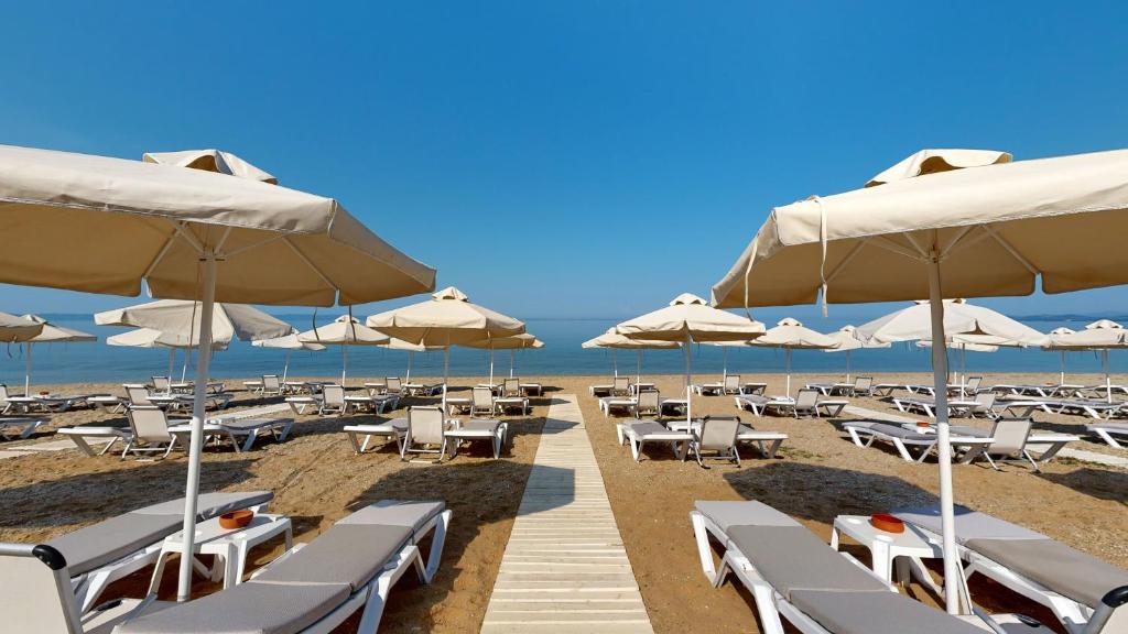 Pludmales skats ar saulessargiem un atpūtas krēsliem, kas izkārtoti gar smilšu krastu. Skaidrs debesis un mierīga jūra radījuši relaksējošu atmosfēru.