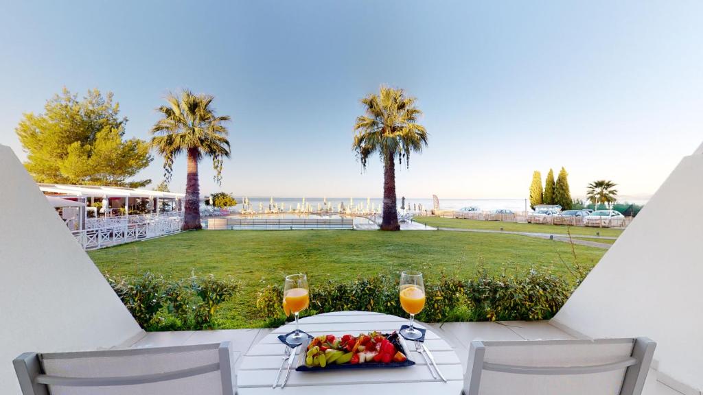 Skats uz jūru no terases ar palmu kokiem un gardu augļu šķīvi, kam blakus ir glāze ar sulu. Ideāla vieta relaksācijai un atpūtai.