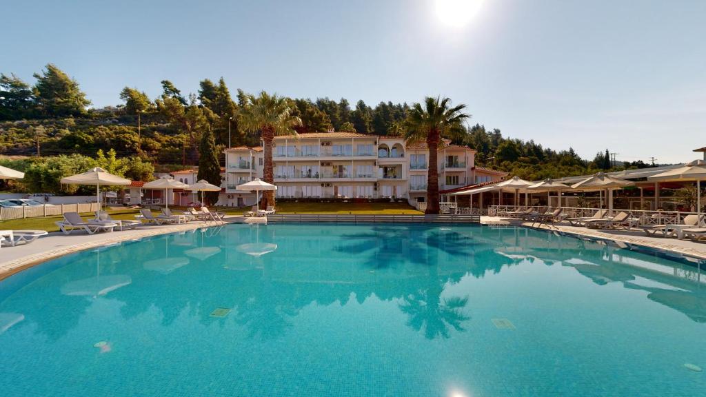 Peldbaseins ar skaidru ūdeni, apkārt palmām un sauļošanās krēsliem, fonā redzama viesnīca ar terasēm. Ideāla vieta relaksācijai un atpūtai.