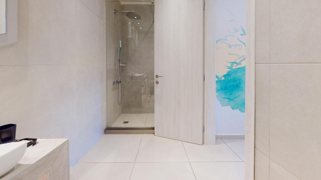 Mūsdienīgs un gaišs vannas istabas interjers ar stikla dušu un krāsu akcentu uz sienas. Vannas istabā ir pelēki flīžu apdares elementi un izsmalcināta izlietne.