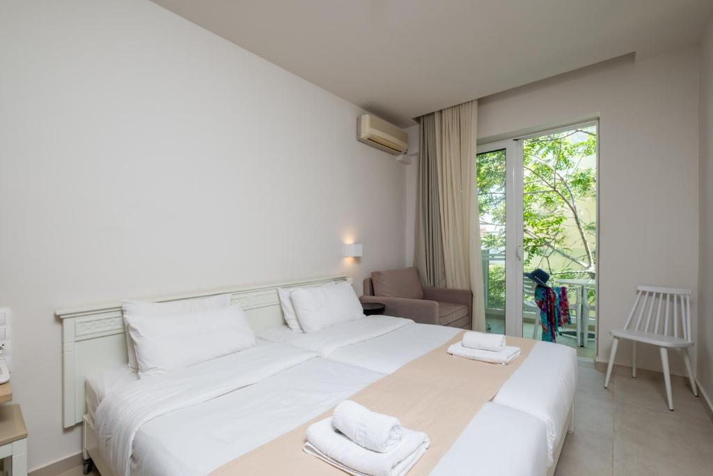 Gaiša un moderna viesnīcas numura interjers ar divguļamo gultu, atpūtas krēslu un balkonu, no kura paveras skats uz dārzu.