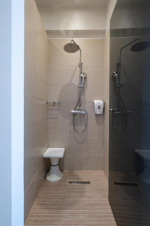 Mūsdienīgs dušas stūrītis ar diviem dušas galviņām un tualeti, izklāts ar gaišiem flīzēm un koka imitācijas grīdu.