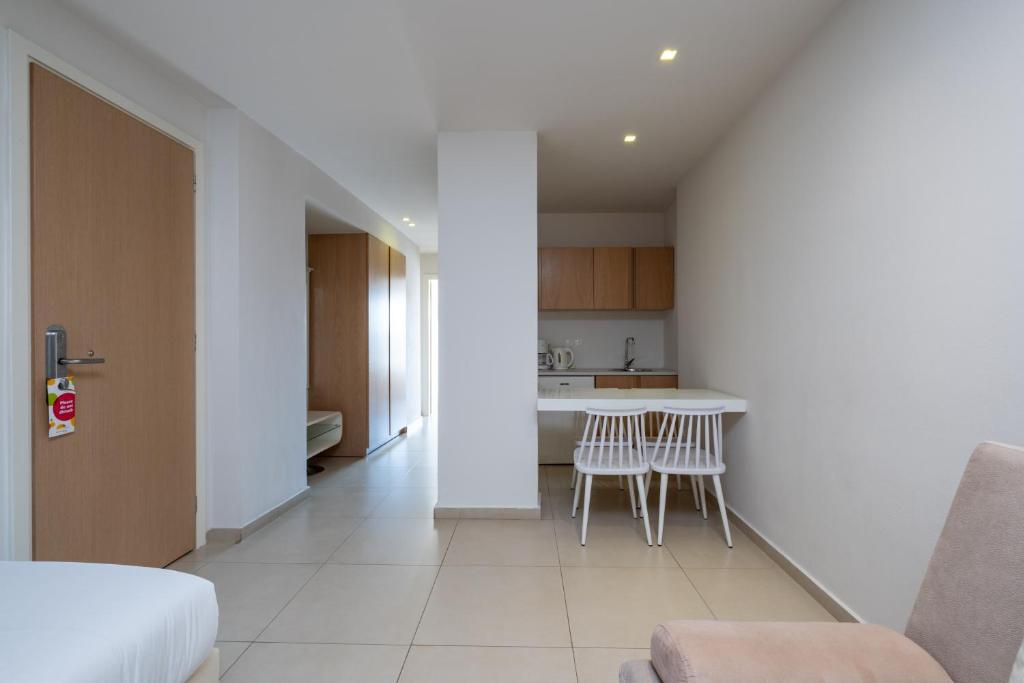 Mūsdienīgs studijas dzīvoklis ar gaišām sienām, koka mēbelēm un nelielu virtuvi. Šajā telpā iekļautas ēdamgalds un krēsli, radot patīkamu un mājīgu atmosfēru.