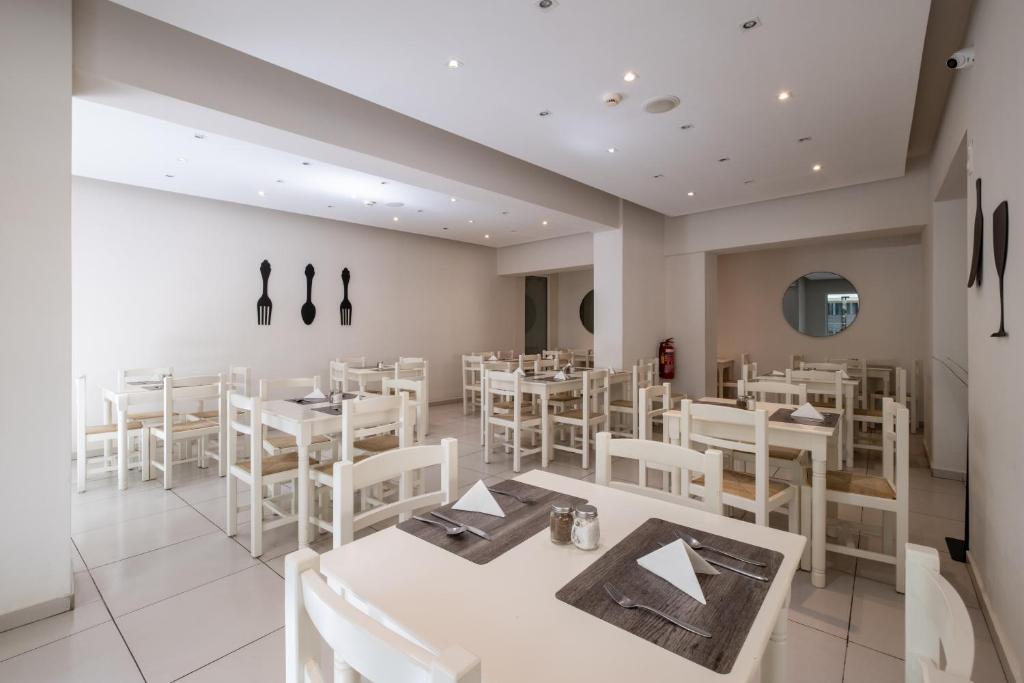 Gaišs un moderns restorāna interjers ar baltām koka mēbelēm, uz galdiem novietoti ēdiena piederumi un servēšanas elementi. Sienās redzami dekoratīvi elementi, kas atspoguļo ēdināšanas tēmu.