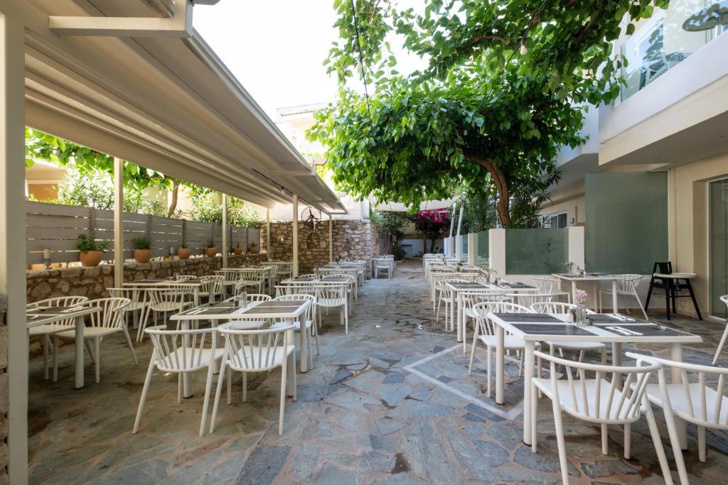 Ārtelpa restorāna terase ar baltiem galdiem un krēsliem, ko ieskauj zaļumi un akmens siena. Gaismas elementi un ziedi piešķir ērtu atmosfēru.