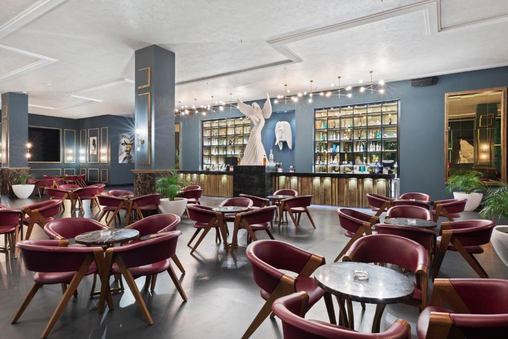 Mūsdienīgs bārs ar elegantiem sarkaniem krēsliem un marmora galdiem, kas iekārtots stilīgā vidē ar mākslas elementiem un plašu dzērienu plauktu.
