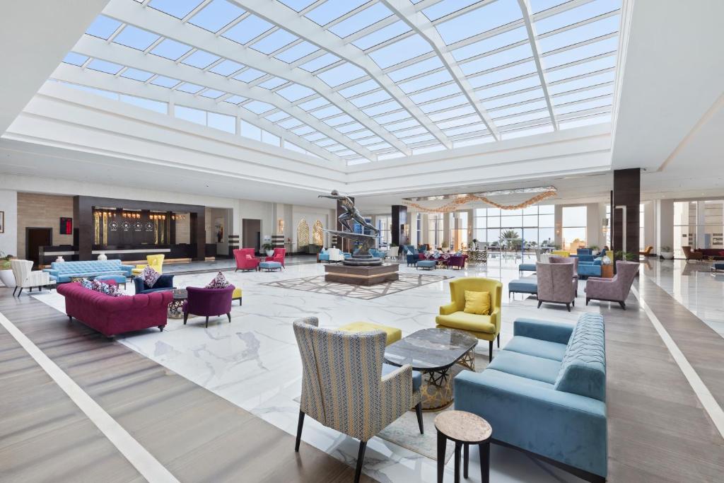 Mūsdienīgs viesnīcas vestibils ar daudzkrāsainām mēbelēm, plašiem logiem un elegantu interjeru, kas rada viesmīlīgu atmosfēru.