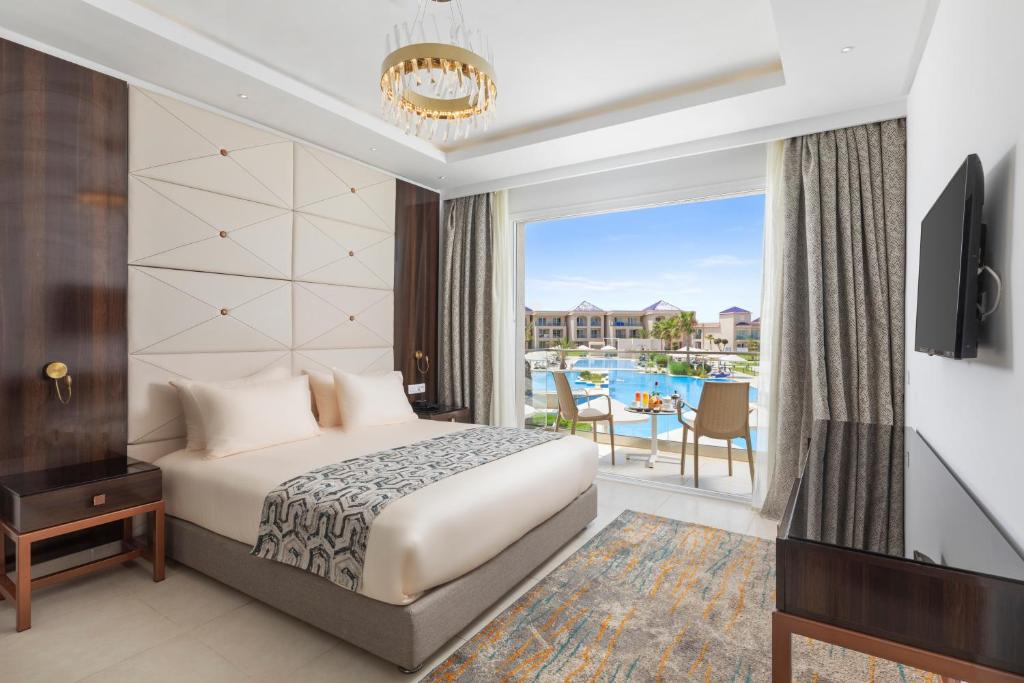 Mūsdienīga viesnīcas istaba ar ērtu gultu, televizoru un skatu uz baseinu caur plašiem logiem. Istabas interjers ir elegants, ar siltām krāsām un moderniem elementiem.