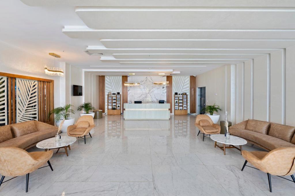 Mūsdienīga viesnīcas vestibilu ar elegantiem dīvāniem, marmora grīdu un stilīgu reģistratūru. Telpa ir apgaismota ar gaismekļiem un dekorēta ar augiem, radot viesmīlīgu atmosfēru.