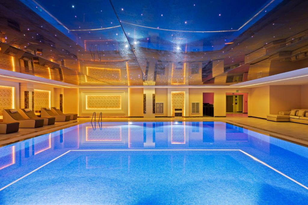 Mūsdienīgs iekštelpu peldbaseins ar spīdīgu zilu ūdeni, apgaismots ar siltām gaismām un elegantu interjeru. Peldbaseina virsma atspoguļo griestus ar zvaigžņu efektu, radot relaksējošu atmosfēru.
