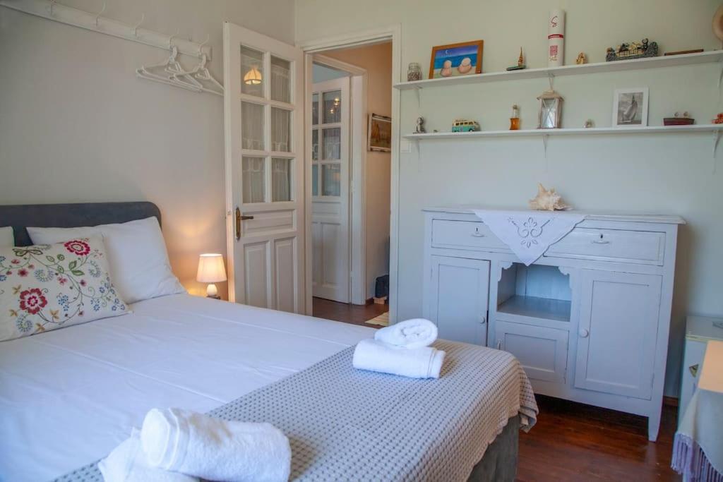 Gaisma un mājīga guļamistaba ar ērtu gultu, dekoratīvām spilveniem un baltām dvielītēm, kas piešķir telpai svaigumu. Uz plaukta redzami dažādi dekoratīvi priekšmeti un krāsainas gleznas, radot patīkamu atmosfēru.