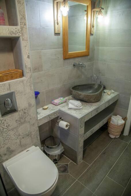 Mūsdienīgs vannas istabas interjers ar akmens izlietni, koka spoguli un minimālistisku dizainu. Telpa ir gaiša un eleganta, izceļot modernus elementus un dabīgus materiālus.