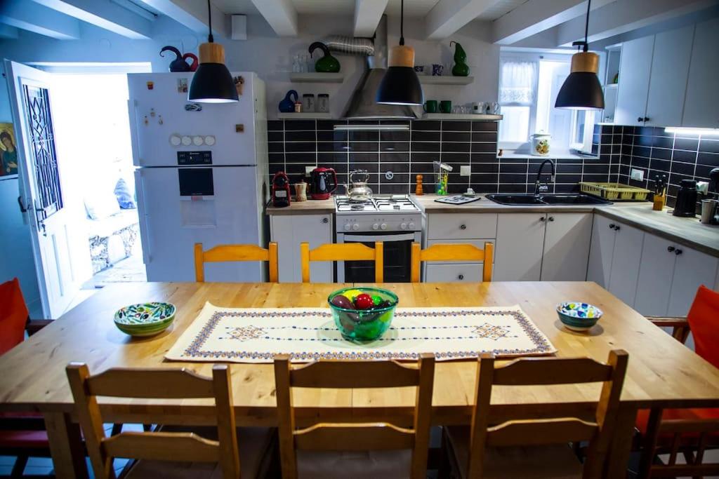 Mūsdienīga virtuve ar koka galdu un krēsliem, melnā flīžu sienā un labi aprīkotu darba virsmu. Uz galda ir dekoratīva servēšanas plate ar augļiem, radot viesmīlīgu atmosfēru.