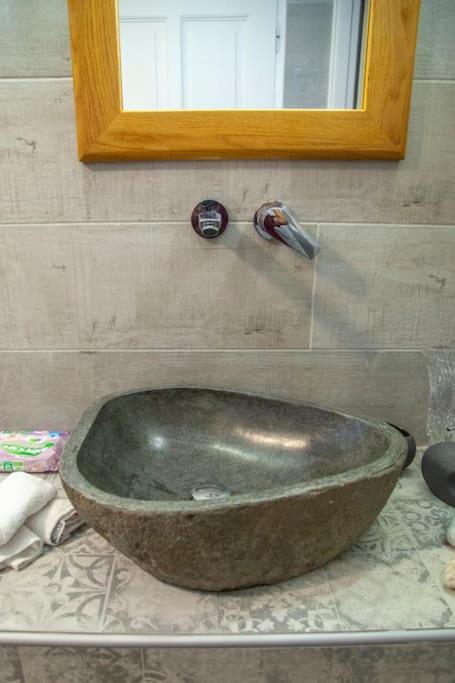 Dabīgā akmens izskata izlietne modernā vannas istabā ar spoguļa rāmīti un hromētiem krāniem.