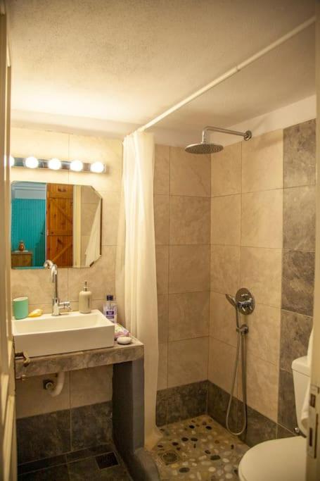 Mūsdienīgs vannas istabas interjers ar dušu, izlietni un spoguli, kas apgaismots ar gaismas ķēdi. Vannas istabā ir flīžu grīda un pieejami higiēnas piederumi.