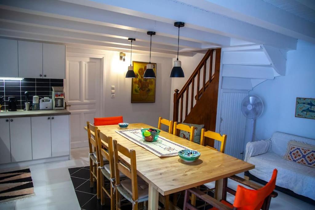 Gaiša un mūsdienīga virtuves un ēdamzāles telpa ar koka galdu un krēsliem, kas apvieno siltas krāsas un funkcionālu dizainu. Telpā ir redzama modernā virtuves iekārta un mājīgs dīvāns.