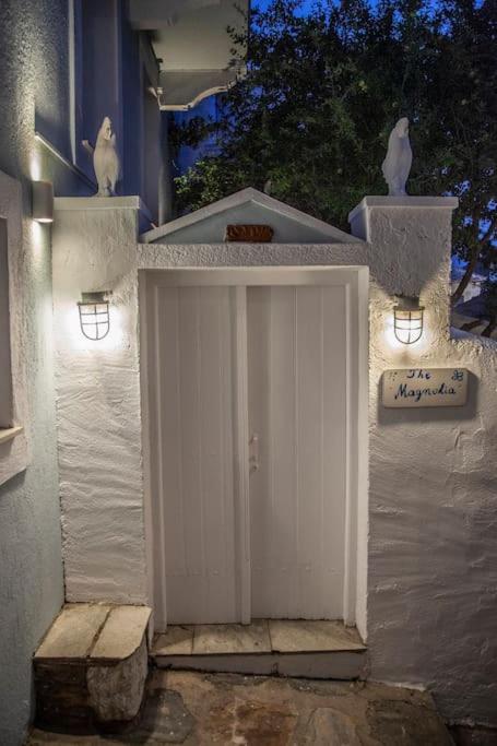 Balta durvju ieeja ar nakts apgaismojumu un dekoratīvām skulptūrām, kas atrodas pie mājas. Uz sienas ir plāksne ar nosaukumu "The Magnolia".
