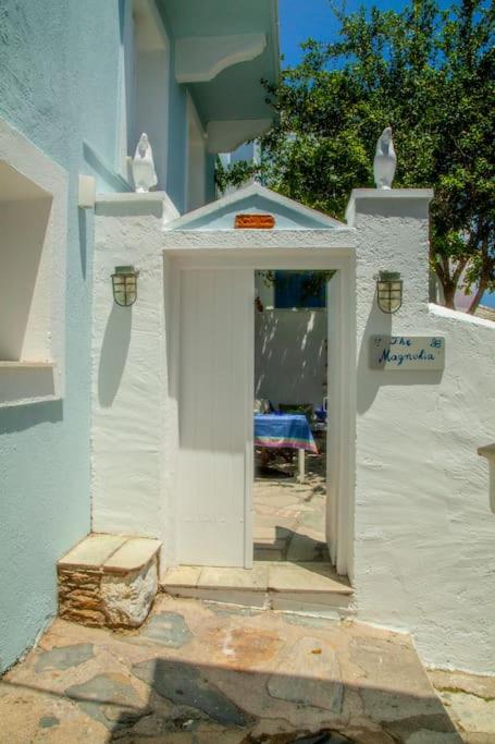 Ieiešana mājīgā ēkā ar gaiši zilu sienu un baltām durvīm, kurā redzams galds ar zilu galdautu. Virs durvīm ir uzraksts "Jāzeps Magnolija".