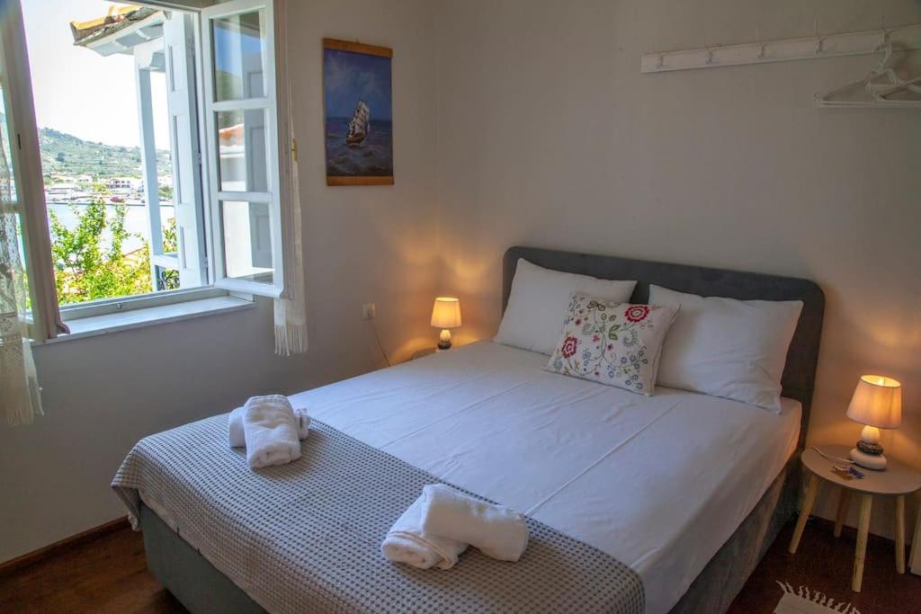 Gaisma un mājīga guļamistaba ar logu, no kura paveras skats uz dabu. Gultā ir dekoratīvas spilveni un dvieļi, blakus ir lampiņas un neliels galdiņš.