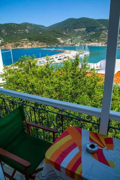 Skats no balkona uz krāšņu jūras piekrasti ar laivām un kalniem fona. Uz galda ir krāsains galdauts un kafijas krūze.