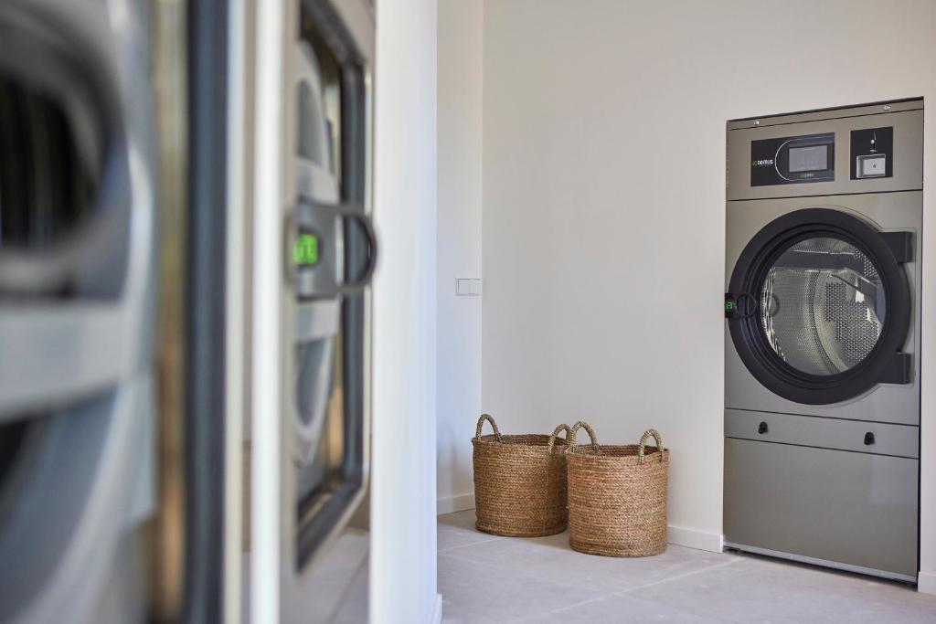 Mūsdienīga veļas mazgājamā mašīna ar žāvētāju, kas novietota gaišā telpā blakus divām pītām groziem.
