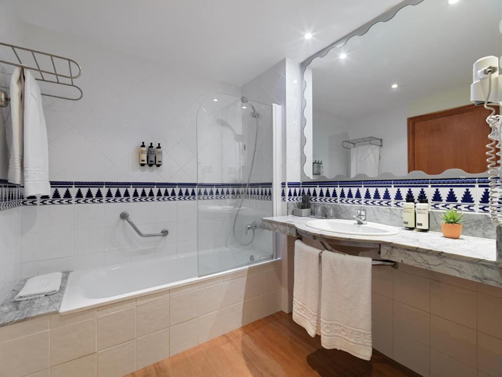 Mūsdienīgs vannas istabas interjers ar vannu un dušu, dekorēts ar zilu un baltu flīžu rakstu. Uz galda atrodas higiēnas līdzekļi un augs.