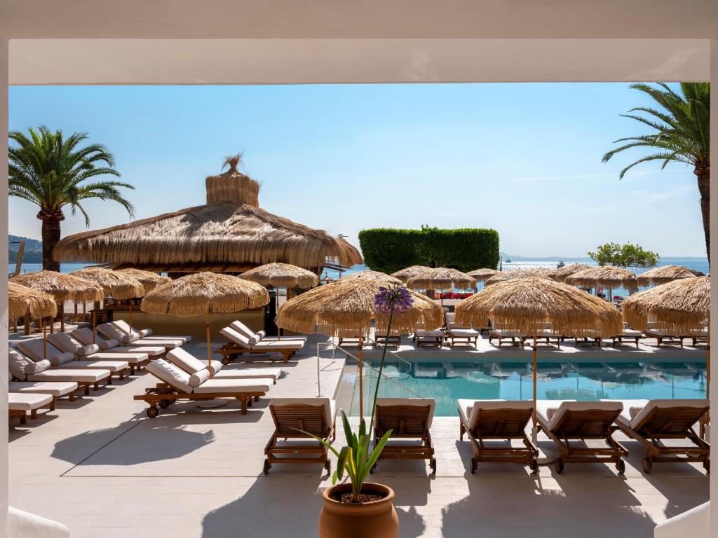 Luksusa viesnīcas baseins ar sauļošanās krēsliem un salmiem, fons ar palmām un jūras skatu. Ideāla vieta atpūtai un relaksācijai.