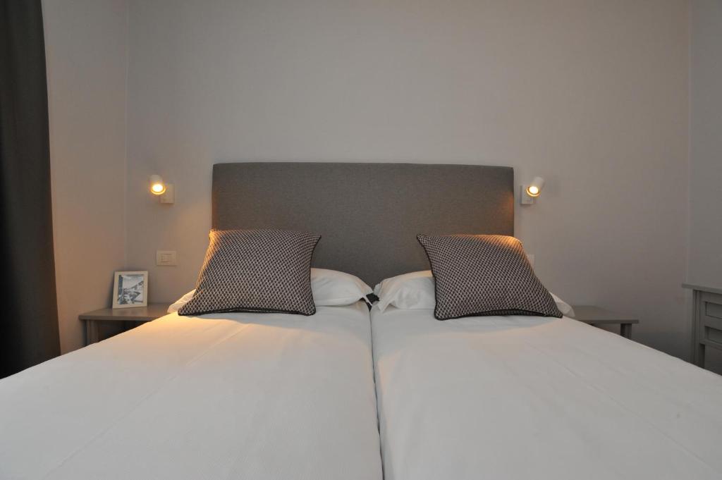 Mūsdienīga guļamistaba ar divām gultām, pelēku galvgali un dekoratīvām spilveniem. Telpā ir siltas apgaismojuma ierīces un koka naktsgaldiņš ar foto rāmīti.