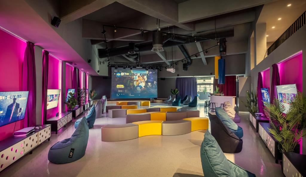 Moderns spēļu telpa ar krāsainiem dīvāniem, lielu ekrānu un televizoriem, kas ir aprīkoti ar spēļu konsolēm. Interjers ir dinamiskas krāsas ar mūsdienīgu dizainu.