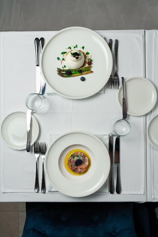 Elegants galda iestatījums ar divām izsmalcinātām ēdiena porcijām. Virsmas centrā redzams pirmais ēdiens ar radošu dekorāciju un otrs ēdiens zem tā.