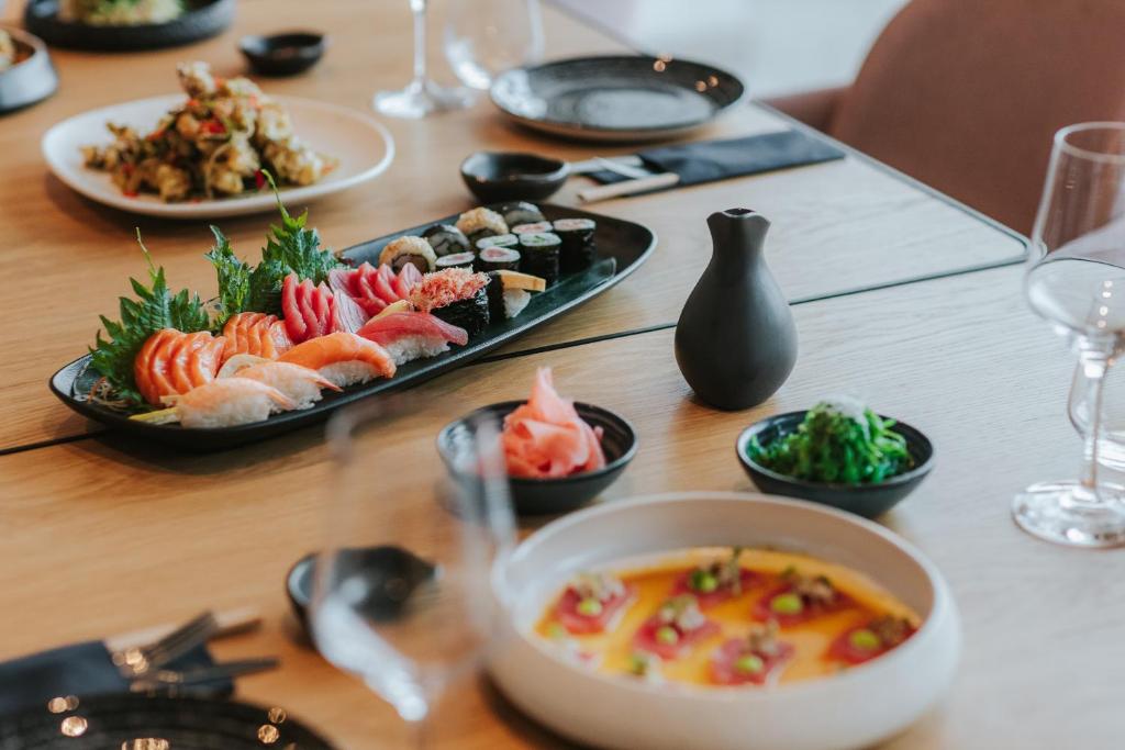 Svaigu suši šķīvī ar dažāda veida zivīm, rīsiem un dārzeņiem, kā arī garnējumi no ingvera un wakame. Uz galda ir arī citas ēdienu šķīvīši un galda piederumi.