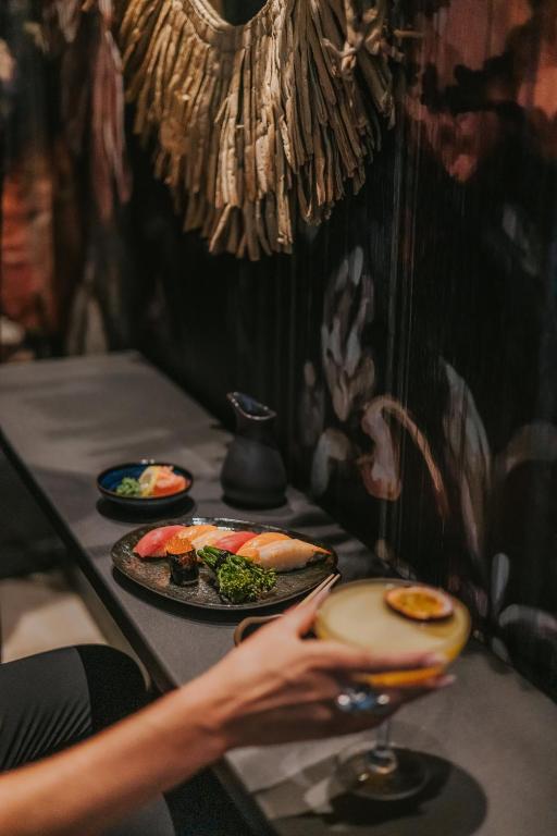 Elegants sushi un kokteiļa komplekts, kas izlikts uz galda, fona rotā eksotiska sienu apdare.