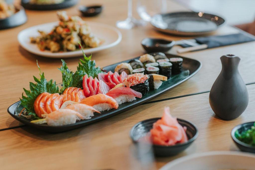 Svaiga sushi un sashimi uz melnas šķīvja, ieskaitot dažādas zivju šķēles un garneles, papildinātas ar zaļumiem. Piemērots izsmalcinātai japāņu ēdiena baudīšanai.