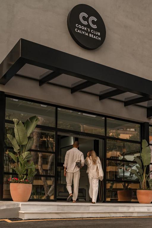 Pāris ieiet modernā viesnīcā "Cook's Club Calvia Beach", kurā ir stilīga arhitektūra un zaļumi pie ieejas.