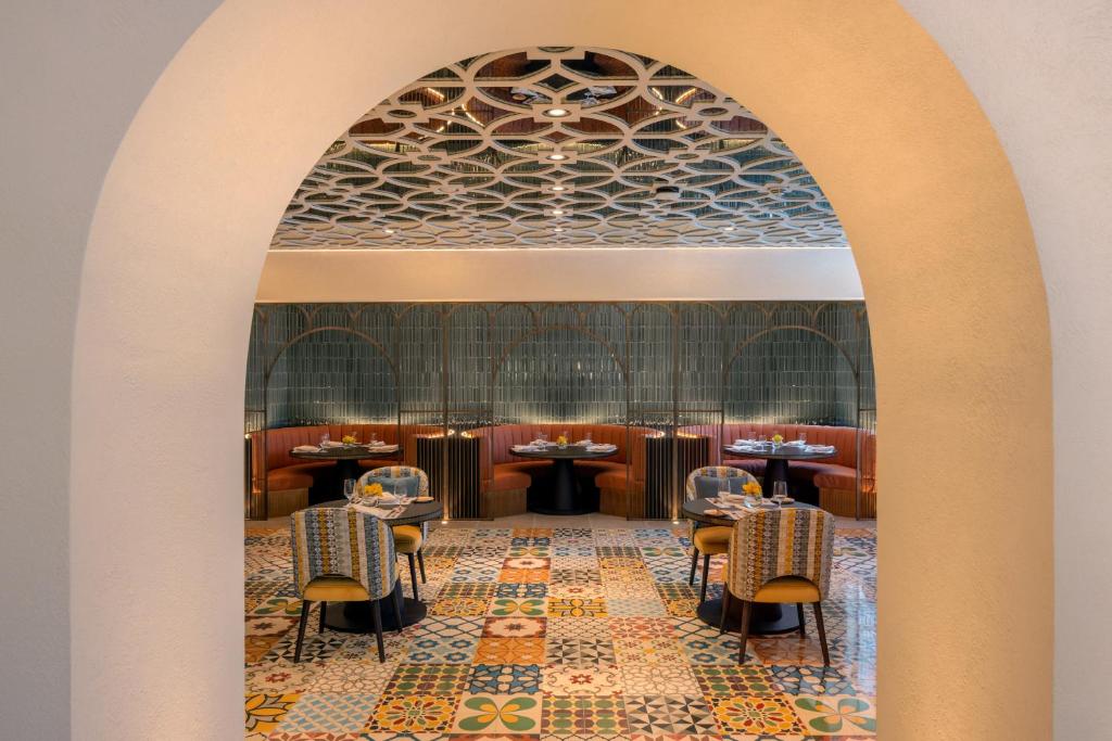 Eleganta restorāna iekštelpa ar krāsainiem flīzēm un stilīgām mēbelēm, veidota ar arku, kas rada siltu un viesmīlīgu atmosfēru. Gaisotne ir moderna un mājīga, ideāla ēdienreizei ar draugiem vai ģimeni.