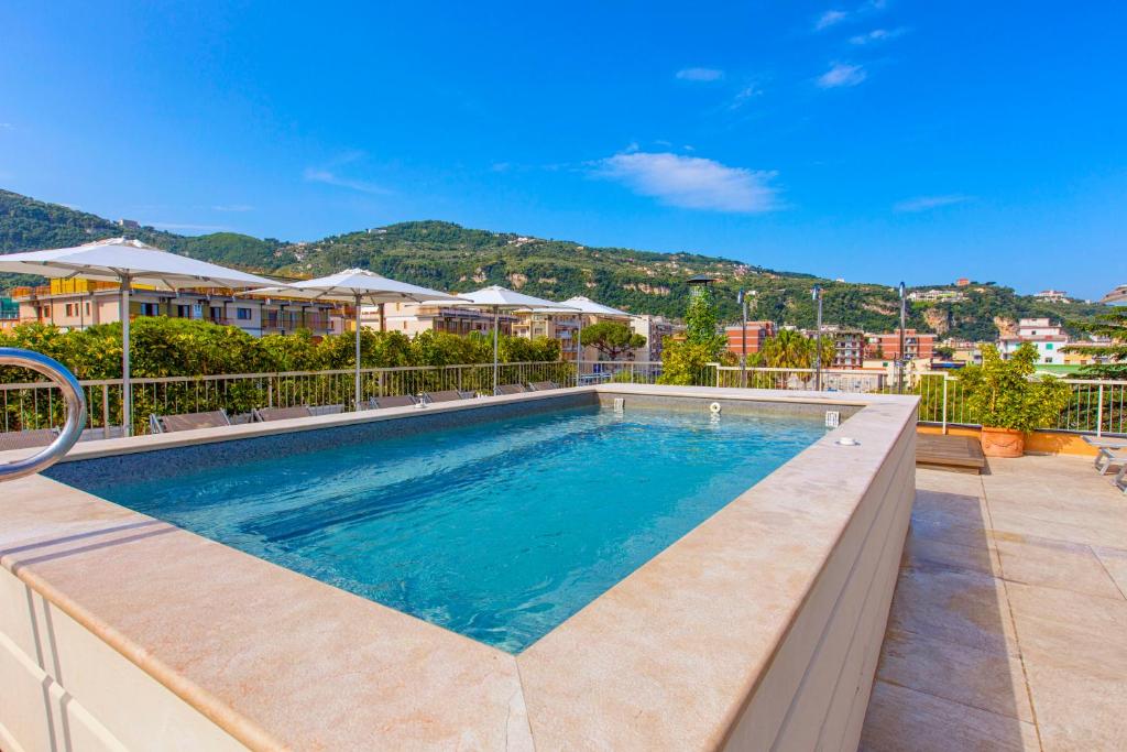 Baseins ar skatu uz kalniem un saulainu debesi, apkārt ir sauļošanās krēsli un saules sētas. Ideāla atpūtas vieta.