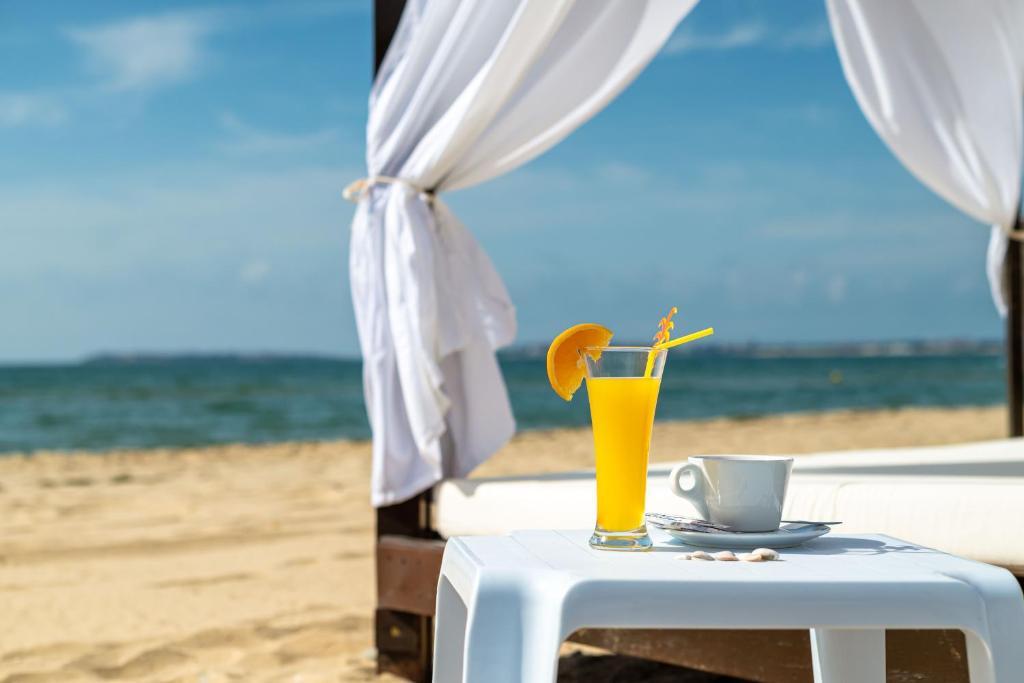 Pludmales ainava ar dzeltenu kokteili un kafijas tase, blakus baltām drānām un zilām debesīm. Ideāla atpūtas aina vasaras dienā.