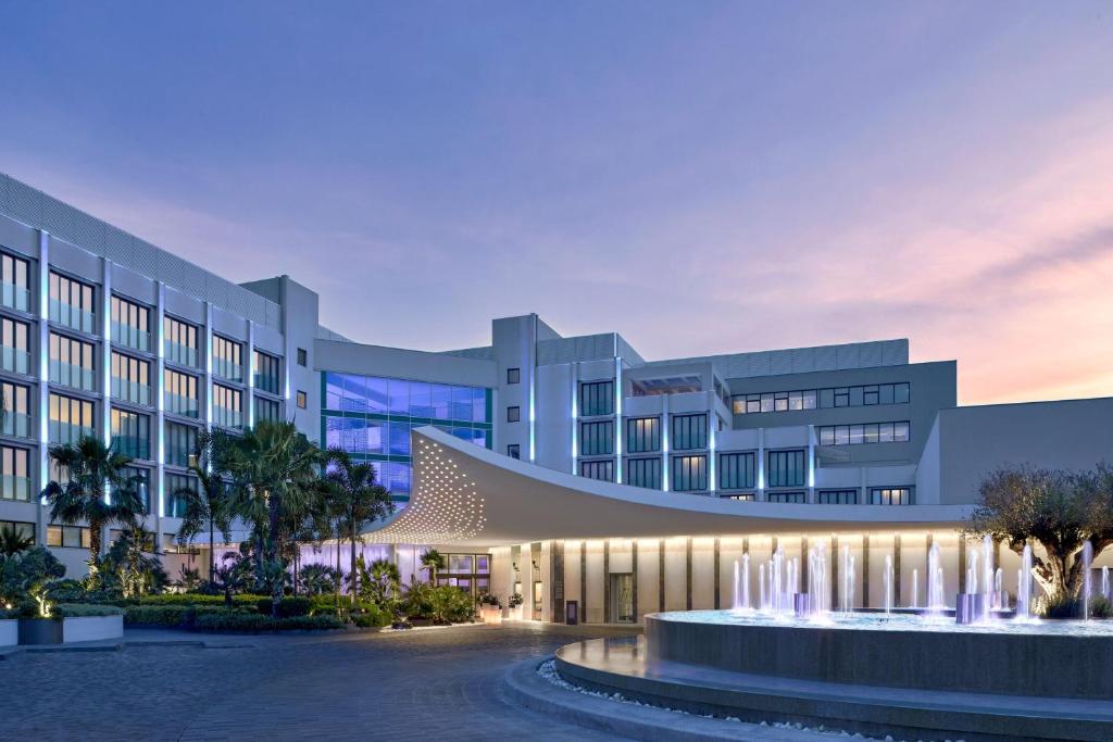 Mūsdienīgs viesnīcas eksterjers ar strūklaku un apzaļumotu teritoriju, kas atspoguļo vakara gaismu. Ideāla vieta atpūtai un relaksācijai.