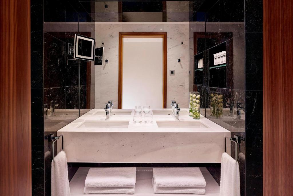 Mūsdienīgs vannas istabas interjers ar divām izlietnēm, spoguļiem un dekoratīvām ziedu kompozīcijām. Eleganta melnā un baltā krāsu kombinācija piešķir telpai stilīgu izskatu.