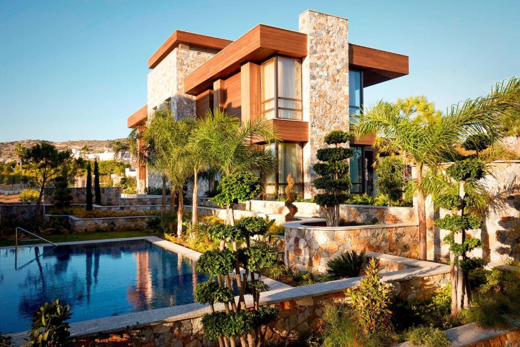 Mūsdienīga māja ar akmens fasādi un koka akcentiem, apkārtne ar zaļām augu kompozīcijām un baseinu.