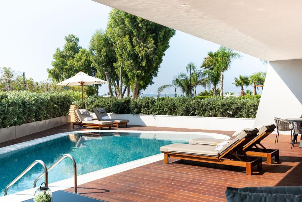 Mūsdienīga terase ap peldbaseinu ar sauļošanās krēsliem un saulessargu, ieskauta zaļiem augiem un palmām. Ideāla vieta relaksācijai un atpūtai.