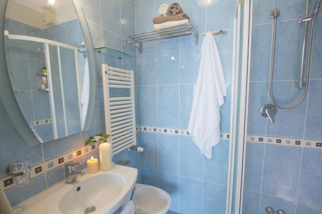 Mūsdienīgs vannas istabas interjers ar zilu flīžu apdari, um pievienotu spoguli, dvieļiem un sveču dekori. Eleganta atmosfēra ar apgaismojumu un praktiskām detaļām.