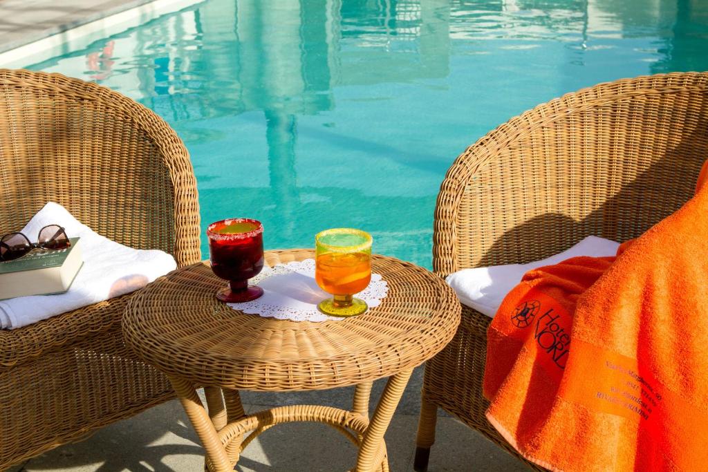 Divas krāsainas dzērienu glāzes uz vīna galda pie peldbaseina, blakus atpūtas krēsliem ar saulesbrillēm un dvieli. Ideāla vieta relaksācijai un vasaras baudīšanai.