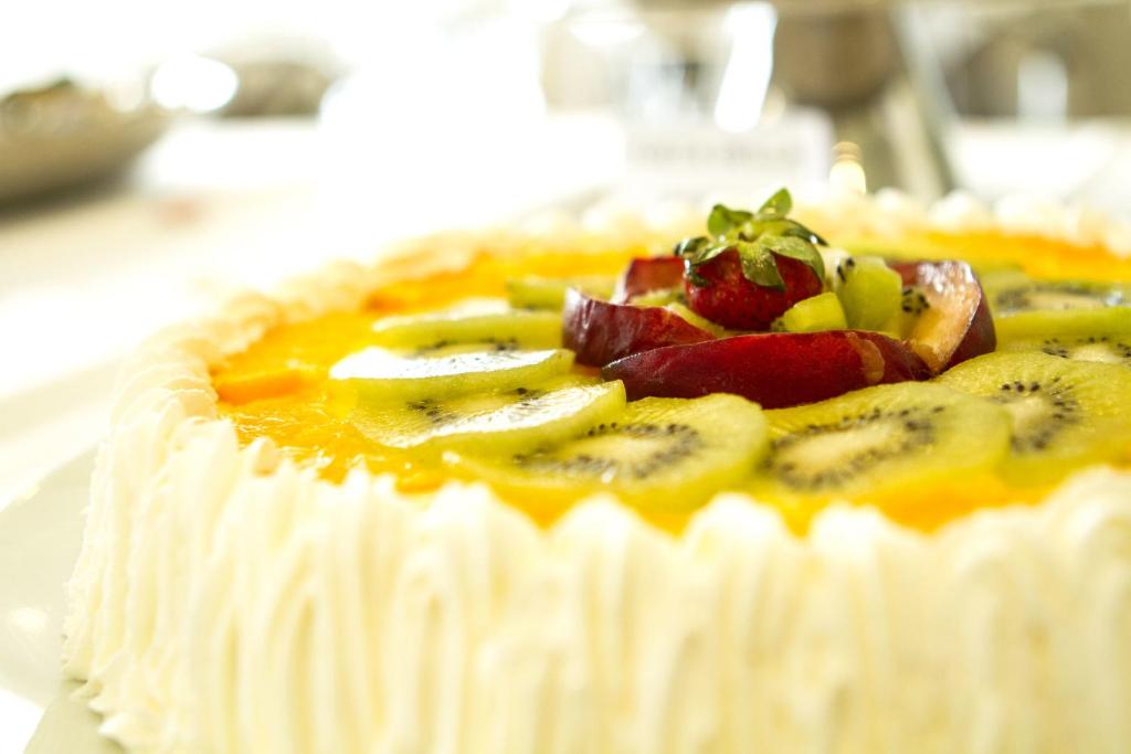 Krēmveida kūka ar augļu dekori, tostarp kivi, zemeņu un ābolu šķēlītēm, uz spilgti dzeltenas krēma pamatnes.