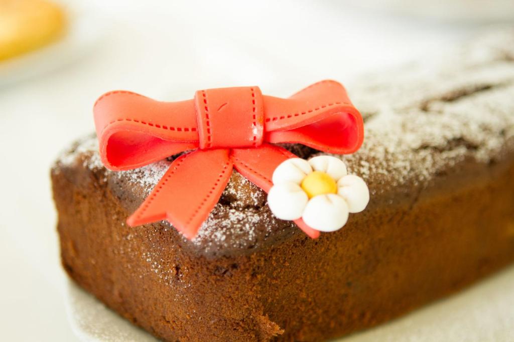 Šokolādes kūka ar sarkanu cukura lentu un ziedu rotājumu, apkaisīta ar pūdercukuru.