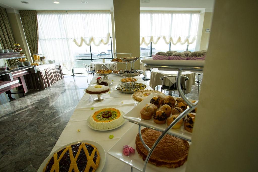 Saldumu bufete ar dažādām kūkām un konditorejas izstrādājumiem, kas novietoti uz galda ar skatu uz logu. Gaisma iekļūst caur aizkariem, radot viesmīlīgu atmosfēru.