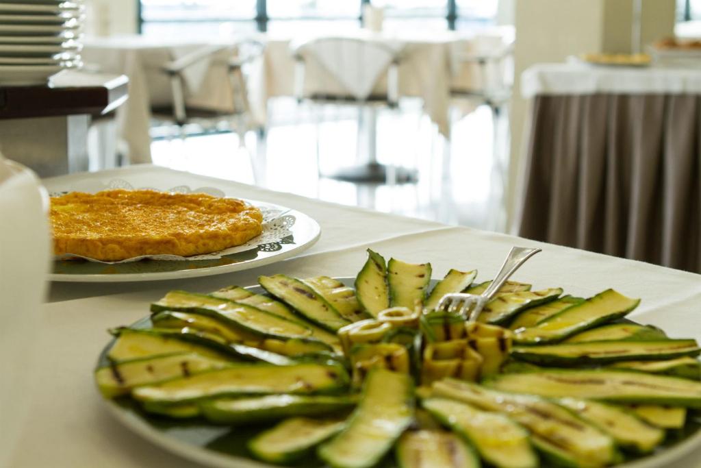 Viena no galda ēdienu izkārtojuma, kurā redzams grilētu cukini šķēlītēm sakārtots uz šķīvja un omlete uz zelta šķīvja.