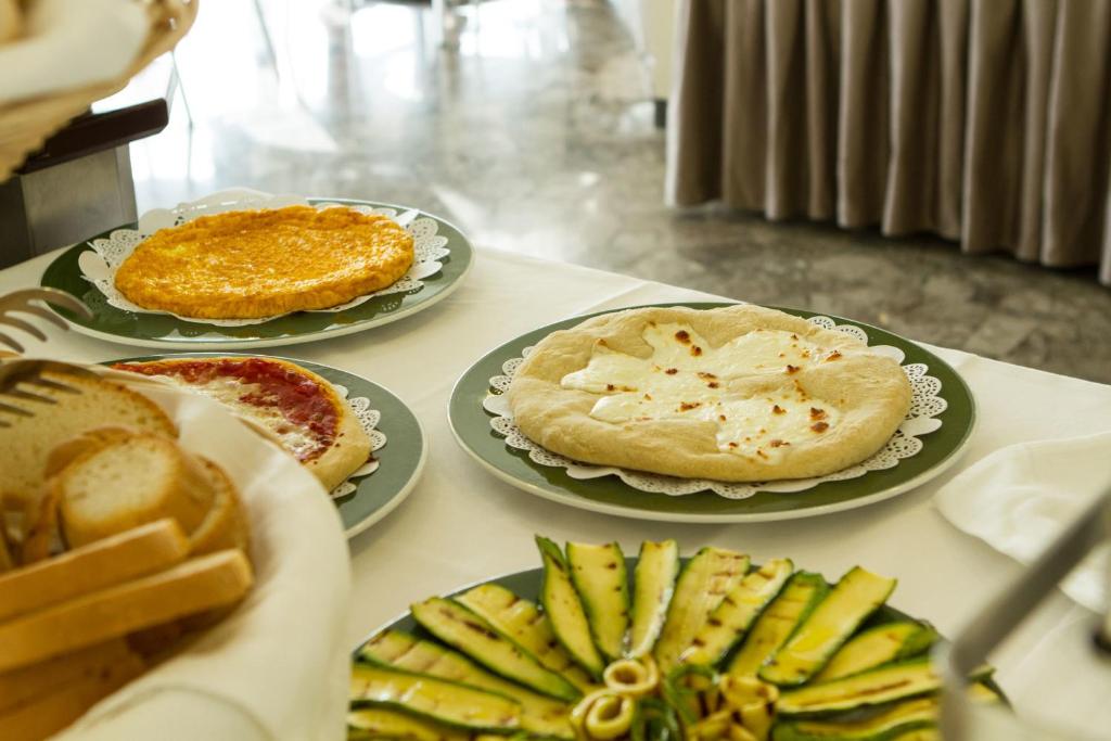 Svaigi cepti pīrāgi un maizītes uz galda, kopā ar dārzeņu šķīvi. Pīrāgi ir ar sieru un tomātu, radot garšīgu brokastu izvēli.