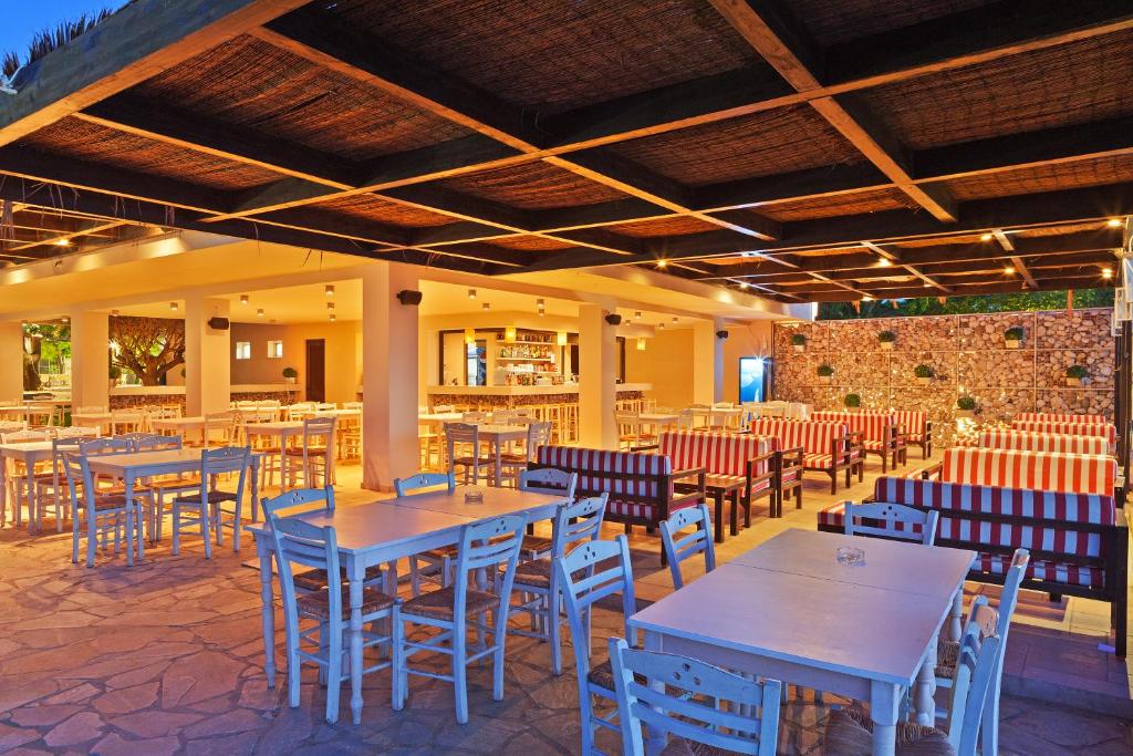 Restorāna iekštelpa ar baltām galdiem un krēsliem, sarkano un balto svītru dīvāniem, siltā apgaismojumā un akmens sienu. Ideāla vieta relaksācijai un ēšanai.