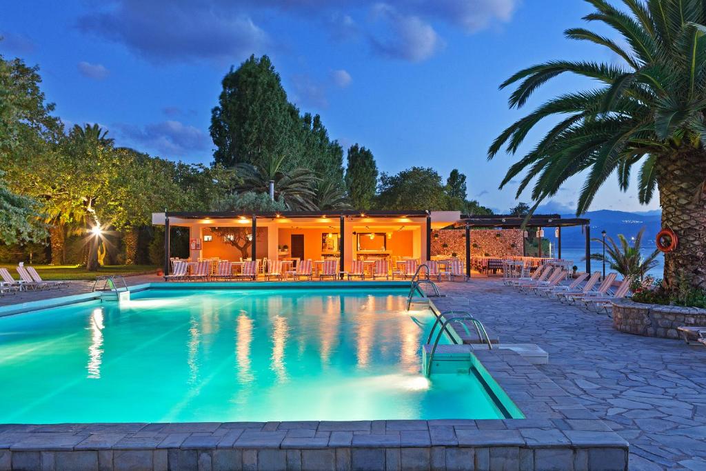 Elegants peldbaseins ar apgaismotu terasi un palmām, apmēram vakarā. Ideāla vieta relaksācijai un atpūtai.